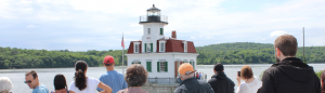 group of people looking out at a lighthouse on the hudson river